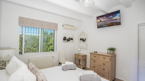 Ein Schlafzimmer mit einem Bett, einem Schminktisch, einem Stuhl, einem Spiegel und einem Fernseher an der Wand.