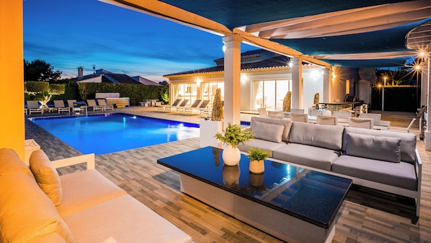 Ein Poolbereich mit einer Couch, einem Couchtisch und Blick auf ein Haus im Hintergrund.