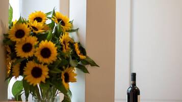 A room with a window, a vase of sunflowers, a bottle, and glasses on the windowsill.