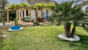 A house with a covered patio, a blue door, and a garden with palm trees and a blue planter.