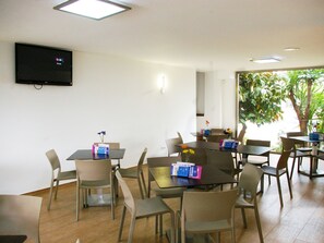 Ein Konferenzraum mit Tischen und Stühlen, einem Flachbildfernseher an der Wand und Blick auf Grünflächen.