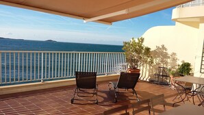 Ein Balkon mit Meerblick, einem Tisch, Stühlen und Topfpflanzen.