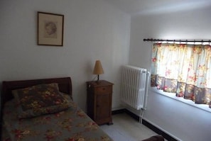 Un dormitorio con cama, mesita de noche, lámpara, radiador y ventana con cortinas.