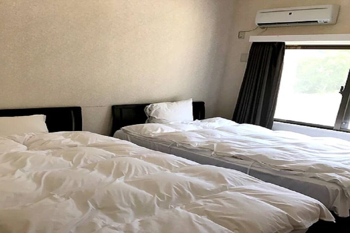 Two beds with white bedding in a room with a window and an air conditioner on the wall.
