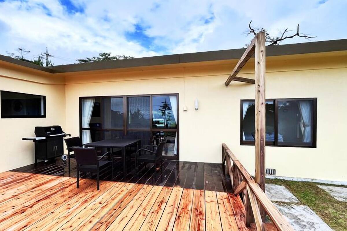 A patio with a wooden deck, a grill, and a table with chairs.