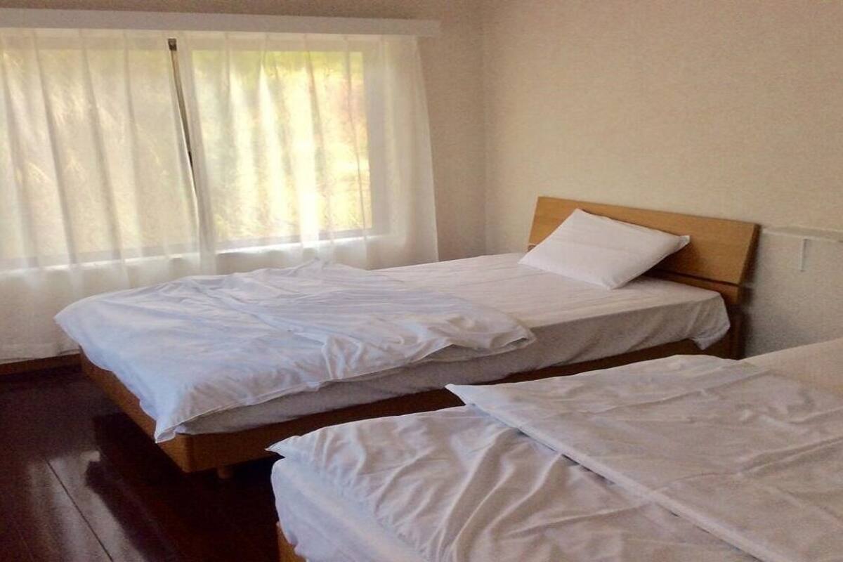 A room with two beds, a window with sheer curtains, and a wooden floor.