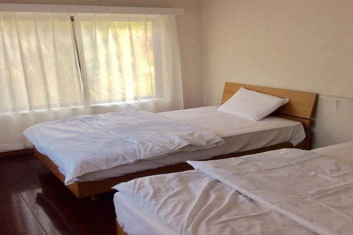 A room with two beds, a window with sheer curtains, and a wooden floor.