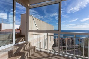 Ein Balkon mit Blick auf das Meer und Gebäude, ein Fliesenboden und ein Geländer.