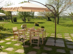 A patio with a table set for dining, surrounded by chairs, under a large umbrella.