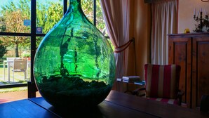 Un jarrón verde de vidrio sobre una mesa de madera cerca de una ventana con cortinas.