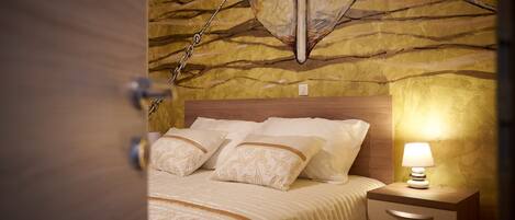 A bedroom with a wooden headboard, a bed with patterned bedding, a bedside lamp, and a wall with a textured design.