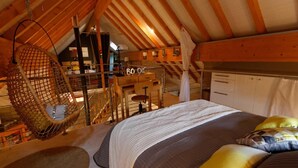 Um quarto de sótão acolhedor com uma cadeira suspensa, uma cama com almofadas e um lance de escadas para um mezanino.
