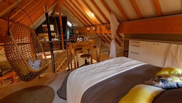 Ein gemütliches Schlafzimmer im Dachgeschoss mit einem Hängekorbsessel, einem Bett mit Kissen und einer Treppe zu einem Erkerraum.