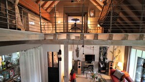 Um amplo loft com mezanino, cozinha e sala de estar com sofá vermelho e mesa de jantar.