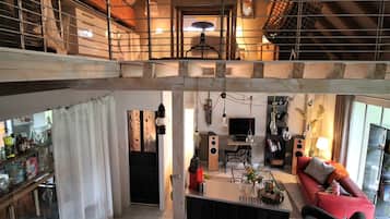 Ruime loft met entresol, keuken en woonruimte met rode bank en eettafel.