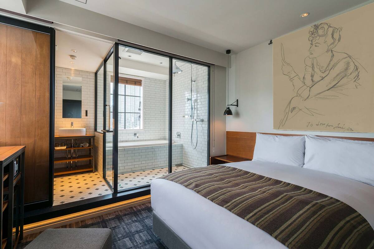 A modern hotel room with a large bed, a bathroom with a bathtub, and a sliding glass door leading to a balcony.