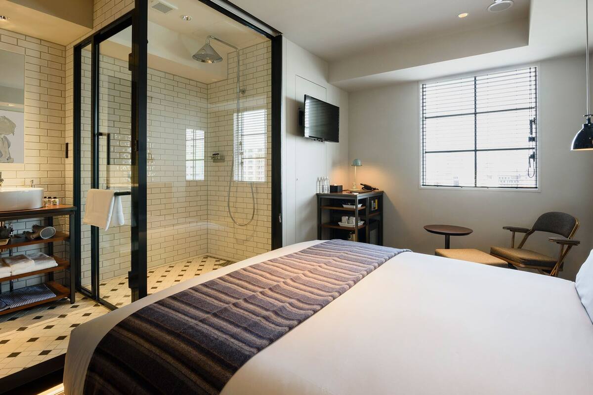A hotel room with a large bed, a shower, a TV, a small table, and a chair.