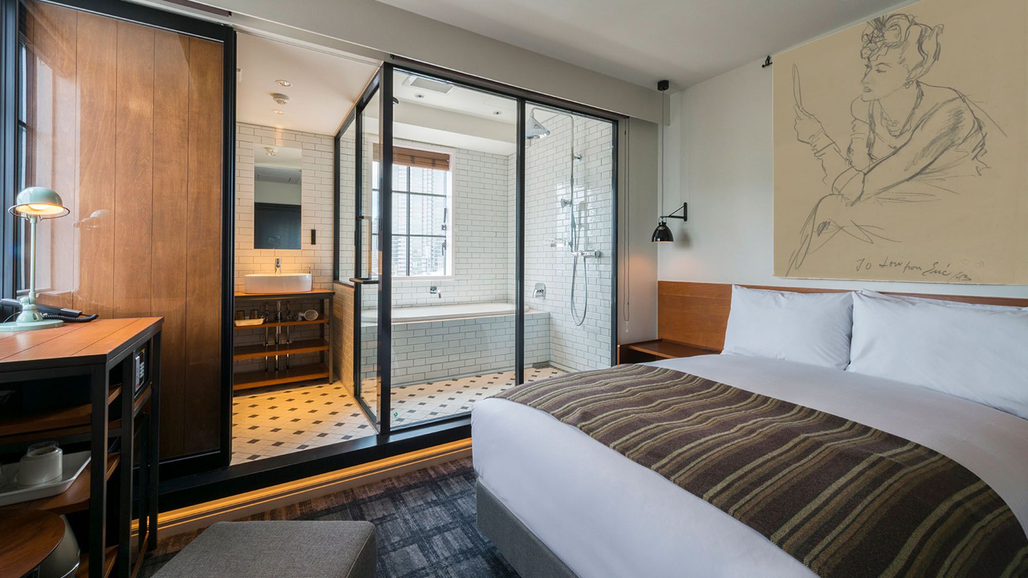 Une chambre d’hôtel avec un lit, un bureau, une salle de bain avec douche et une grande fenêtre.