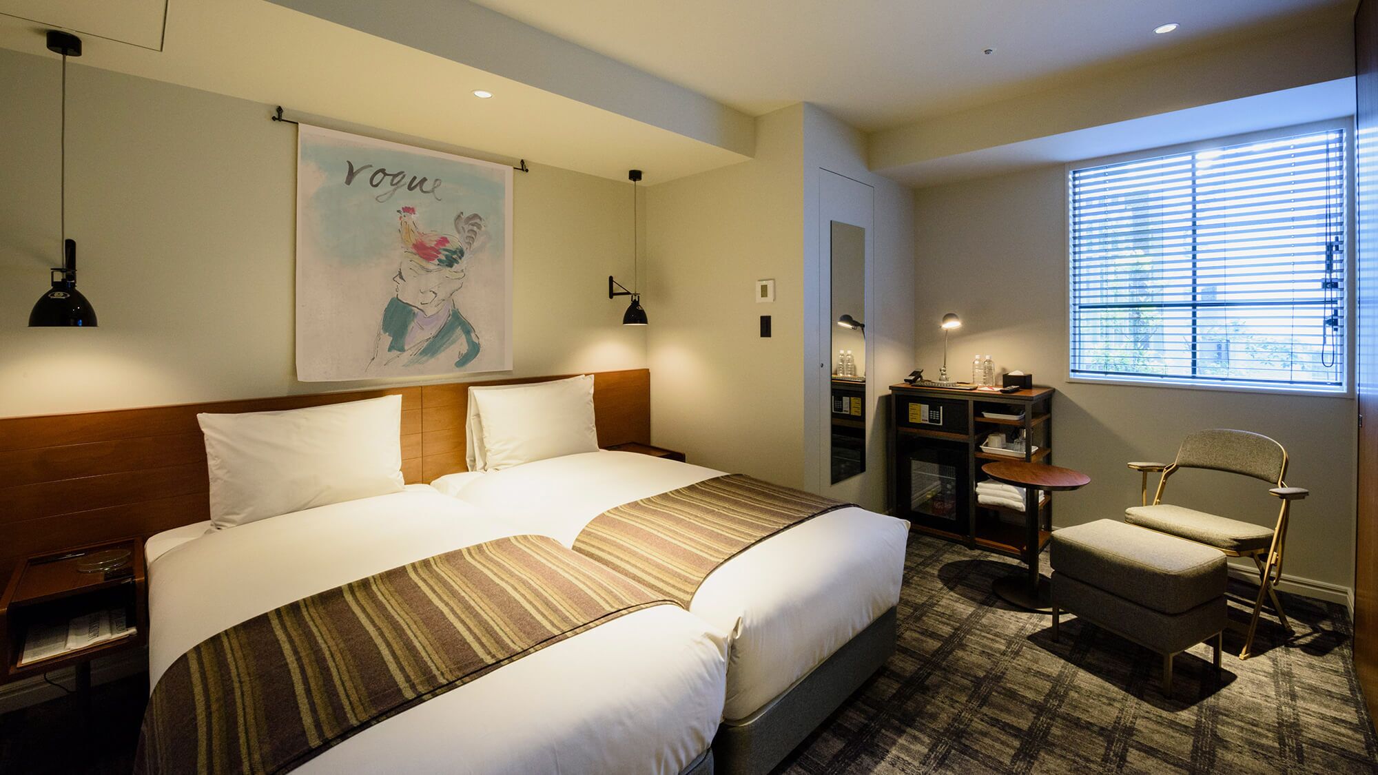 Une chambre d’hôtel avec un lit, un bureau, une chaise et une fenêtre avec des stores.
