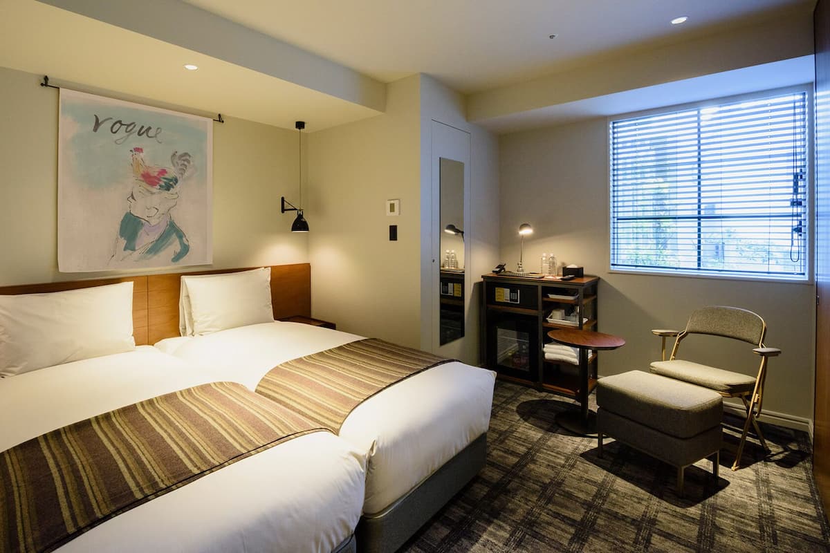 A hotel room with a bed, a desk, a chair, and a window with blinds.
