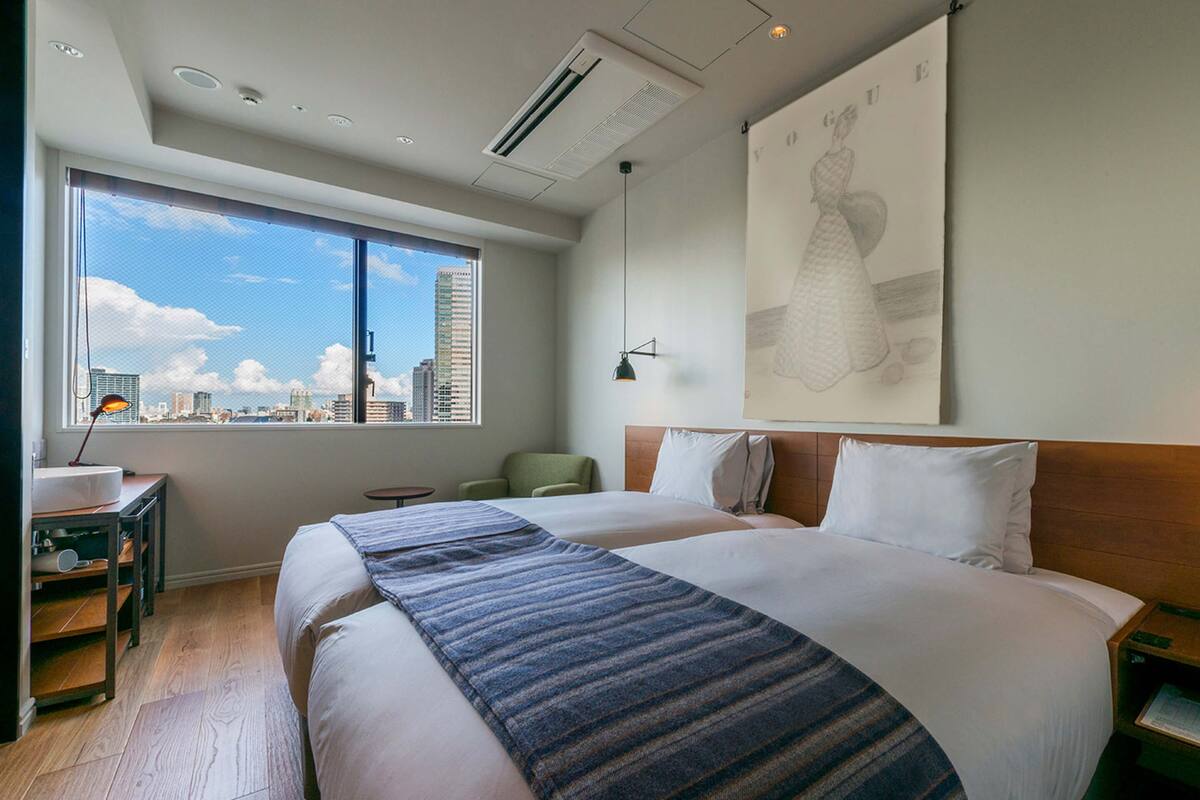 A hotel room with a large bed, a desk, a chair, and a window with a city view.