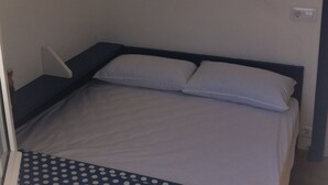 A small, single-bed room with a simple bed, a small bedside table, and a wall-mounted shelf. - LIKE BEING ON BOARD OF A BOAT AT SEA (MAHON)