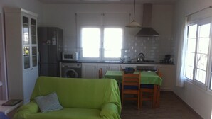 A compact living space with a green sofa, a dining table with chairs, a kitchen area with appliances, and a window providing natural light. - LIKE BEING ON BOARD OF A BOAT AT SEA (MAHON)