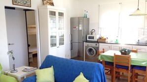 A compact living space with a blue sofa, a dining table with chairs, a washing machine, a microwave, and a cabinet with glass doors. - LIKE BEING ON BOARD OF A BOAT AT SEA (MAHON)