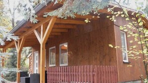 Une cabane en bois dotée d’un porche couvert, de fenêtres et d’une zone délimitée par une clôture.