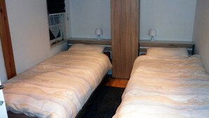 Une petite chambre, de taille modeste, avec deux lits simples, chacun doté d’une t ête de lit en bois et d’une table de chevet avec une lampe.