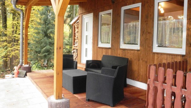 Un espace extérieur aménagé, abrité et doté de mobilier en osier, de poutres en bois et offrant une vue sur une zone boisée.
