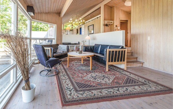 A cozy living room with a sofa, armchair, and coffee table, featuring a large window and a decorative rug. - 4 bedroom beautiful home in Asnæs (Asnæs)