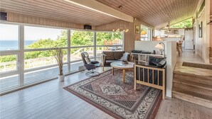 A spacious living area with large windows, a cozy seating area, and a kitchen in the background. - 4 bedroom beautiful home in Asnæs (Asnæs)
