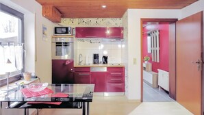 A compact kitchen with a microwave, oven, and sink. There is a dining table with a glass top and red napkins. The kitchen has a wooden ceiling and pink cabinets. - Lovely apartment in brensbach ot wersau (Brensbach OT Wersau)