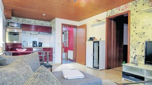 A modern living room with a sofa, a coffee table, and a TV stand. There is a kitchen area with a microwave, oven, and cabinets. A refrigerator is visible in the background. - Lovely apartment in brensbach ot wersau (Brensbach OT Wersau)