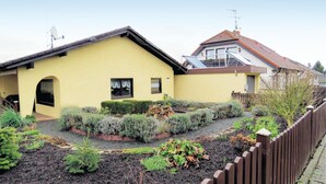 A yellow house with a sloped roof, a small porch, and a garden with various plants and a wooden fence. - Lovely apartment in brensbach ot wersau (Brensbach OT Wersau)
