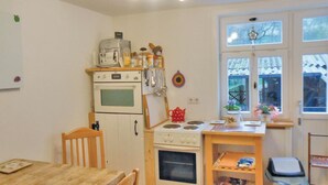 Una cucina compatta con un tavolo di legno, due forni, un piccolo bancone e una finestra vista giardino.