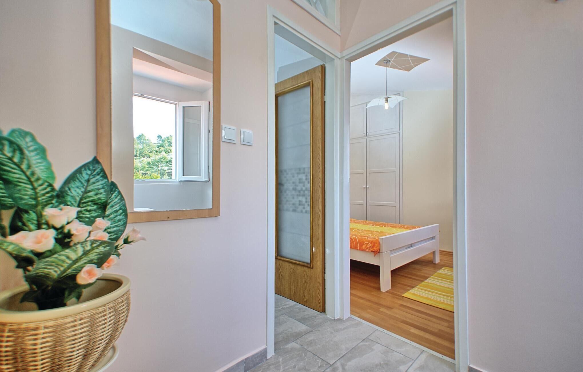 Ein Flur, der in ein Schlafzimmer mit Bett, Kleiderschrank und einer Topfpflanze führt.