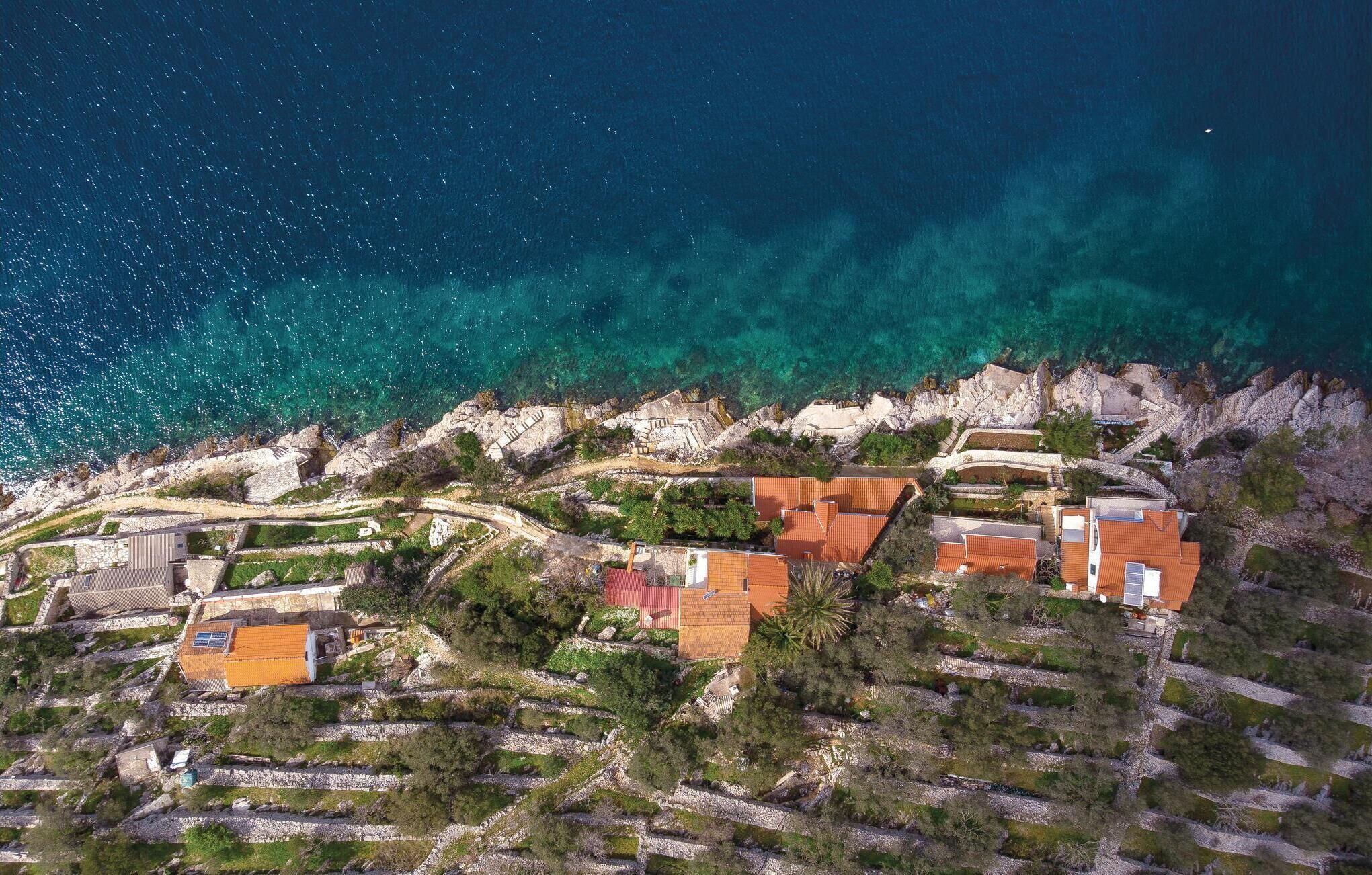 An aerial view of a coastal village with terraced houses, clear turquoise waters, and rocky cliffs.