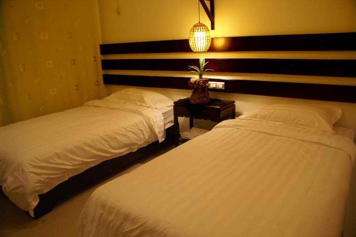 A hotel room with two single beds, a nightstand with a lamp, and a wall-mounted shelf.