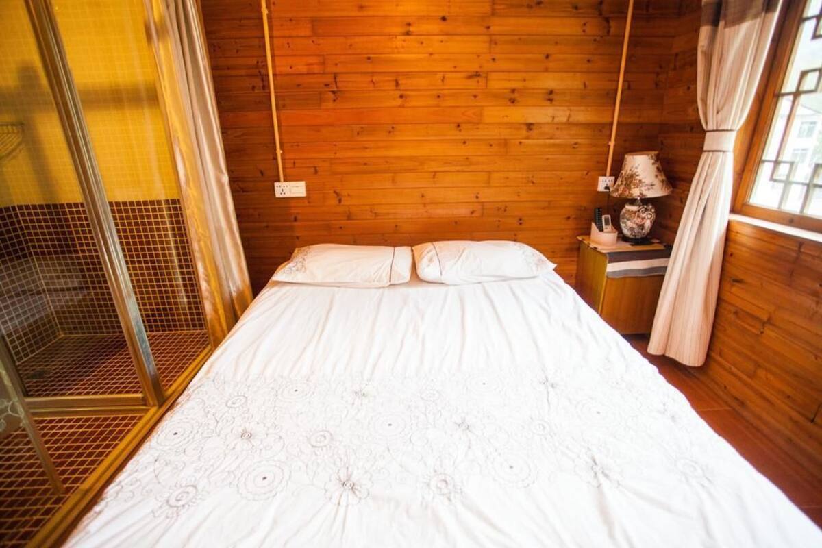 A wooden room with a bed, a nightstand, and a window with curtains.