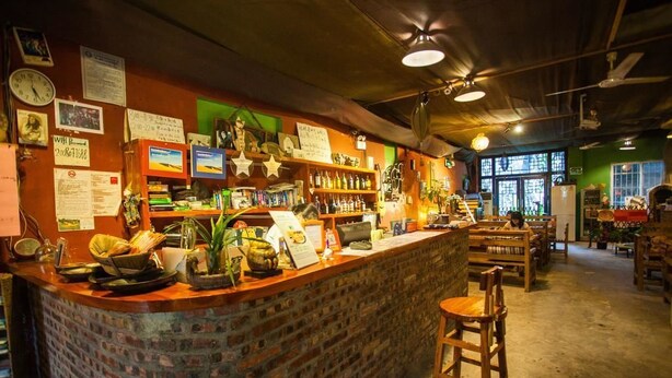 A bar area with a brick counter, wooden chairs, and various items on shelves. - The Old Place In't Youth Hostel (Guilin)