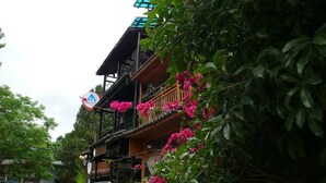 A multi-story building with balconies, surrounded by lush greenery and pink flowers. - The Old Place In't Youth Hostel (Guilin)