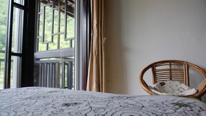 A room with a bed, a wicker chair, and a window with curtains. - The Old Place In't Youth Hostel (Guilin)