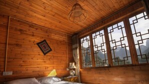 A wooden cabin bedroom with a bed, a hanging light fixture, a window with a geometric pattern, and a view of mountains. - The Old Place In't Youth Hostel (Guilin)