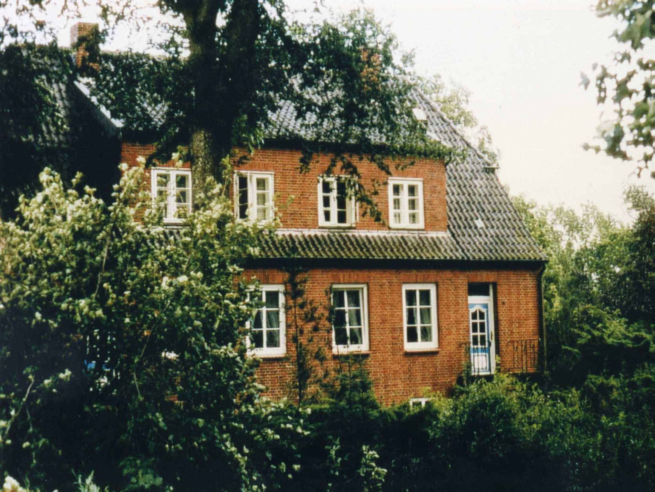 Een tweelaags bakstenen huis met ramen met witte kozijnen, een opvallende voordeur en een pannendak.