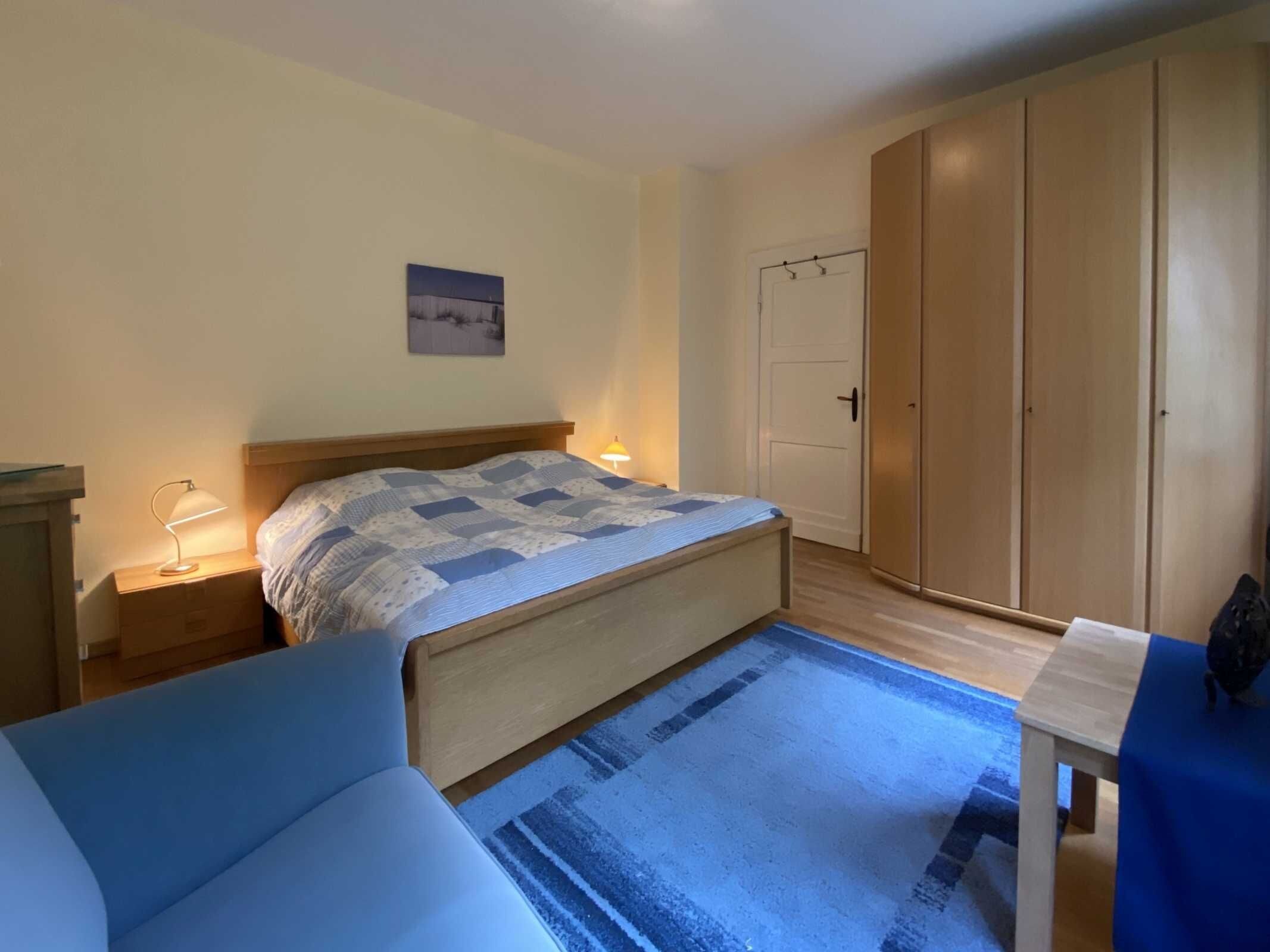 A bedroom with a bed, bedside lamps, a wardrobe, and a small table.