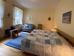 Um quarto com cama, escrivaninha, cadeira, cômoda e janela com cortinas.