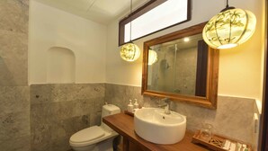 Een badkamer met een marmeren wand, een houten wastafelmeubel, een witte wastafel en twee hanglampen.