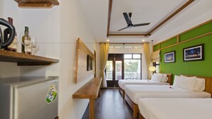 Een hotelkamer met twee bedden, een houten bankje, een koelkast en een plafondventilator.